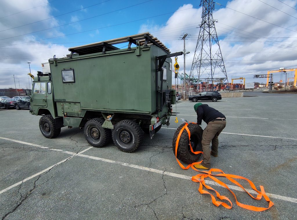 Foto vom Volvo am Hafen in Halifax während Chris einen Gurt um das Ersatzrad tüdelt.