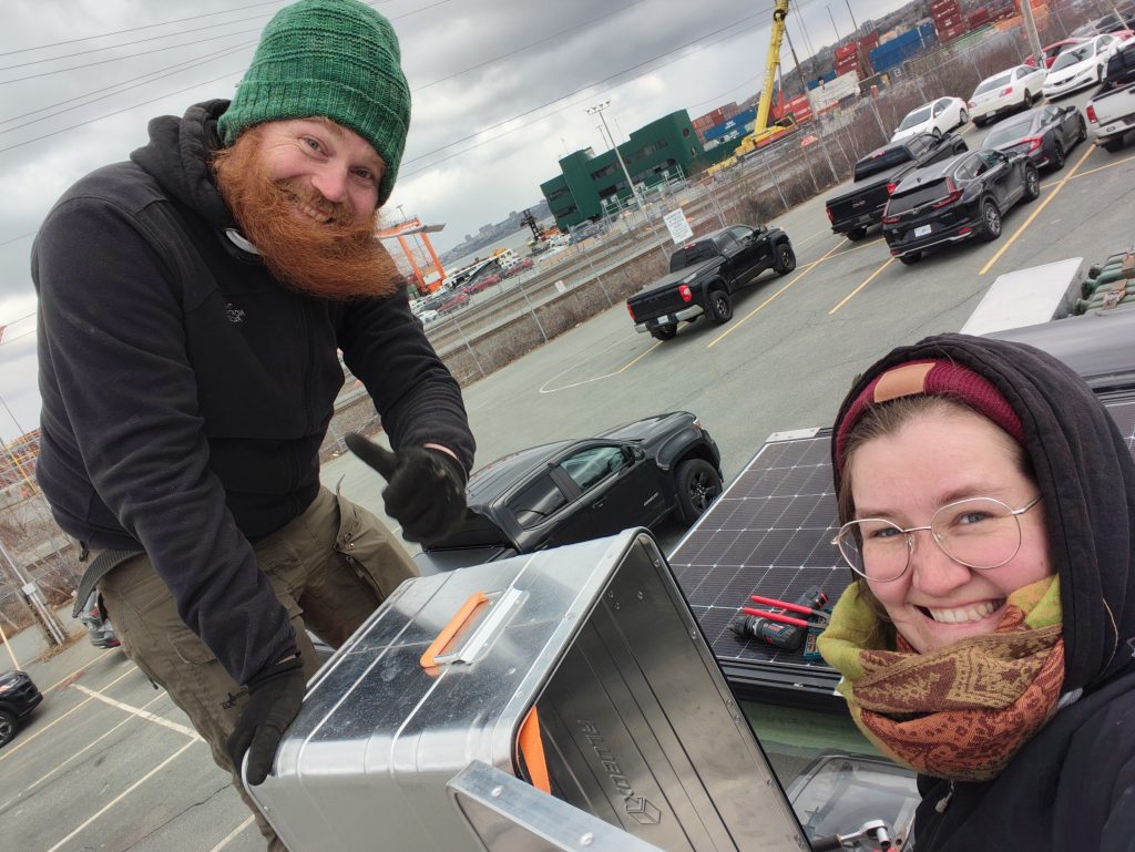 Foto von uns beiden auf dem Dach vom Volvo, Chris mit wehendem Bart, während wir die Staukisten anbringen.
