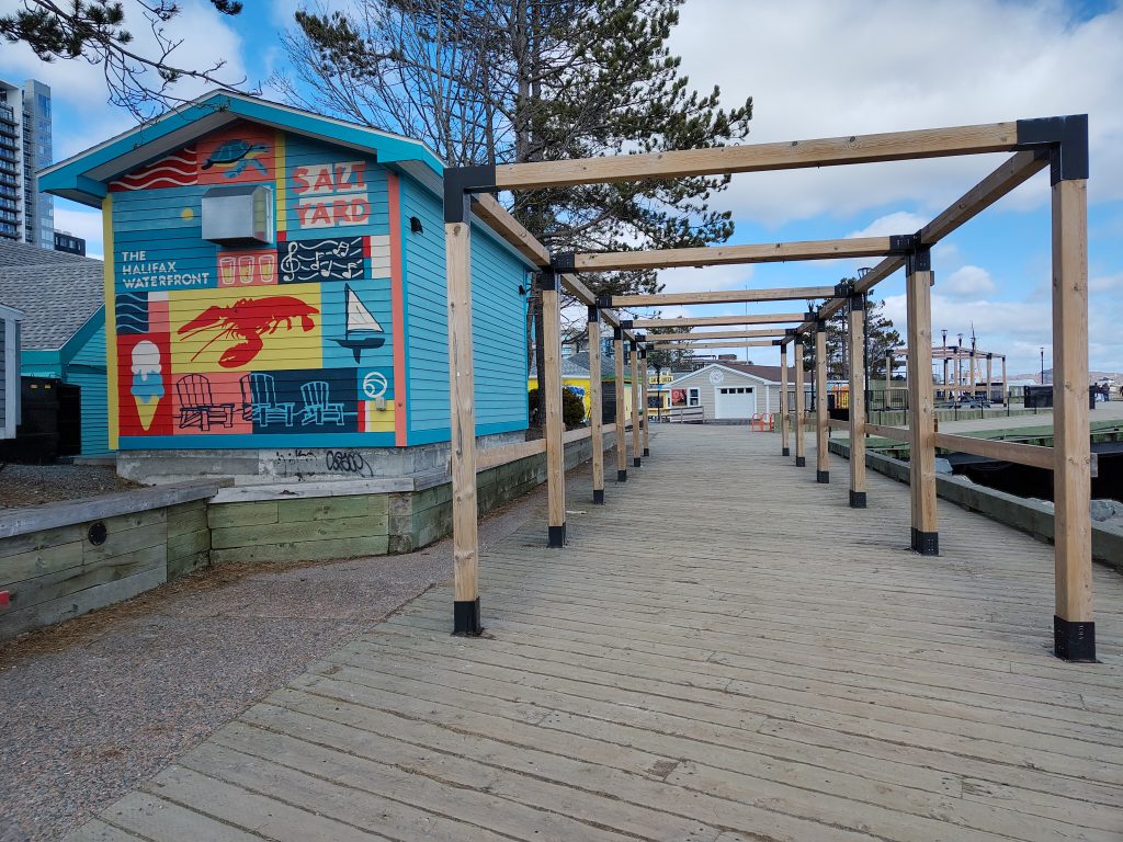Foto vom Eingang der Waterfront in Halifax. Graffiti von einem Hummer an einem der Container neben dem Holzdielenweg.
