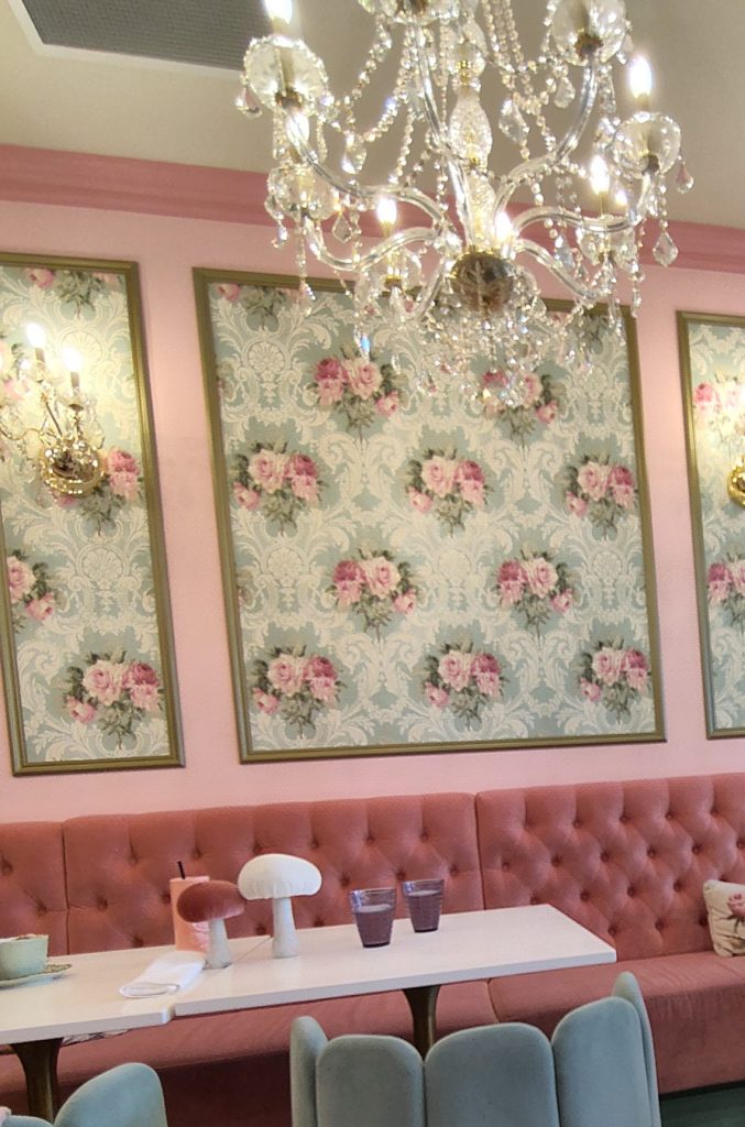 Foto der Inneneinrichtung vom Café Crème: Blumentapete, viel rosa und Kronleuchter.