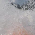 Foto: Wasserspritzer reichen bis über den Kopf beim Rafting auf einem Fluss und Bäume im Hintergrund