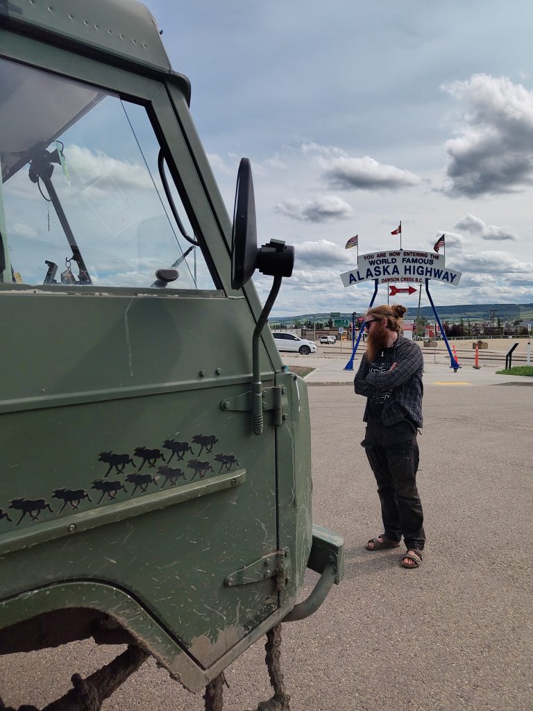 Chris vor dem Alaska Highway Schild, redet mit anderen Reisenden über den Volvo