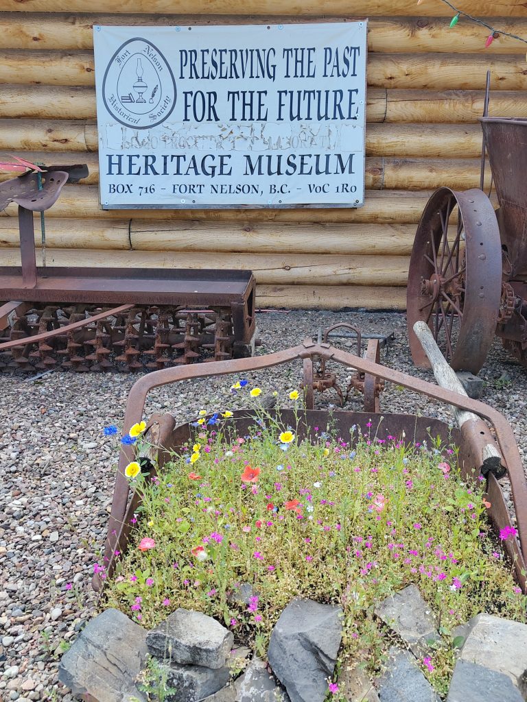 Blumenbett in Baggerschaufel. Schild mit Museums Motto: Preserving the Past for the future