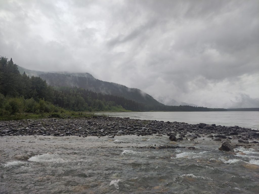 Die regen Wolken hängen sehr tief über dem Fluss und verhüllen die Berge
